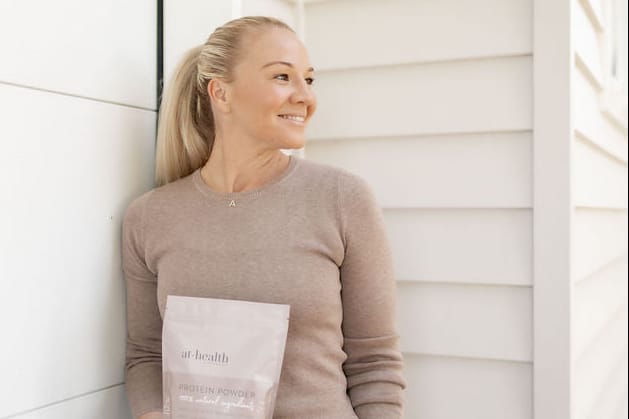 Woman holding protein powder 'At Health' 